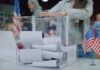 Person casting a ballot into a clear box at a polling station