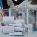 Person casting a ballot into a clear box at a polling station