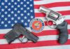 Woke State’s New Gun Permit System Is Insane Two handguns and NRA emblem on an American flag