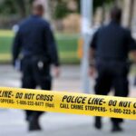 Police officers walking past caution tape at a crime scene