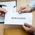 Hands holding a resignation letter envelope across a desk