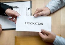 Hands holding a resignation letter envelope across a desk