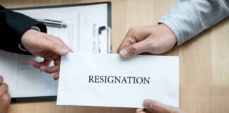 Hands holding a resignation letter envelope across a desk
