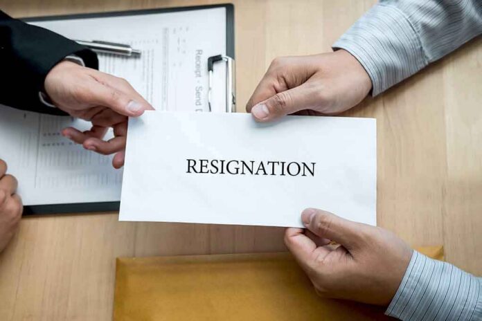 Hands holding a resignation letter envelope across a desk