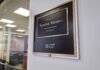 Senators Bodyguard RANSACKS Her Home Office door plaque with gold trim outside a glass-walled conference room