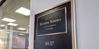 Office door plaque with gold trim outside a glass-walled conference room