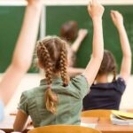 students raising hands in a classroom