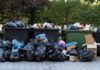 Overflowing dumpsters with piles of trash bags and cardboard