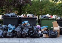 Overflowing dumpsters with piles of trash bags and cardboard