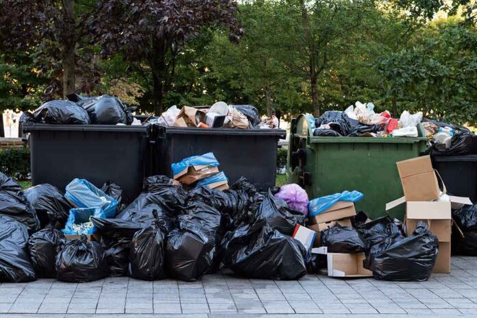shutterstock_1509489287 Overflowing dumpsters with piles of trash bags and cardboard