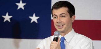 Man speaking into a microphone in front of an American flag