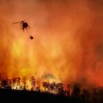 State of Emergency DECLARED — Mass Evacuations Underway Helicopter fights massive wildfire over burning forest