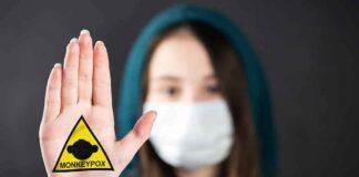 Person in mask holding up palm with monkeypox warning patch