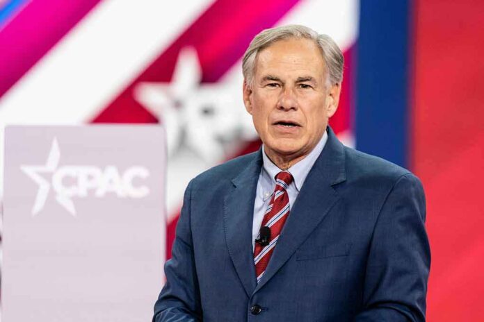 Greg Abbott speaking on stage in a blue suit with a red striped tie