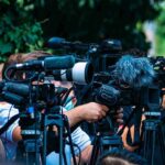 TV news cameras crowding together at an outdoor event