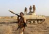 soldier carrying rocket-propelled grenade launcher in front of armored vehicle