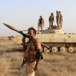 soldier carrying rocket-propelled grenade launcher in front of armored vehicle