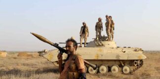 soldier carrying rocket-propelled grenade launcher in front of armored vehicle