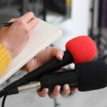 DSA to Illegal Aliens: ‘You Don’t Have to Have Papers’ Journalist holding two microphones while writing in a notebook