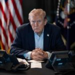 Trump Takes Wrecking Ball to JFK Memorial Person in suit seated at table with telephones