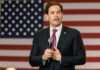 Rubio Schools Media on Trump’s White House Ban man in suit speaking with microphone before American flag