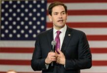 Rubio Schools Media on Trump’s White House Ban man in suit speaking with microphone before American flag