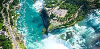 Aerial view of a large turquoise river plunging over a horseshoe-shaped waterfall
