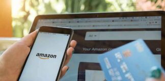 person holding smartphone with Amazon app and credit card near laptop