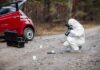 Forensic investigator photographing evidence near a red car on a rural road