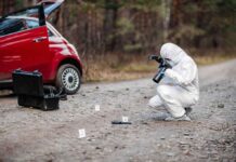 Forensic investigator photographing evidence near a red car on a rural road