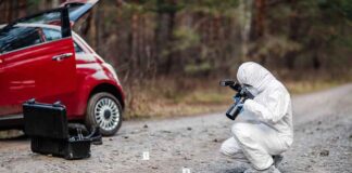 Forensic investigator photographing evidence near a red car on a rural road