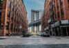 Street view with bridge between two brick buildings.
