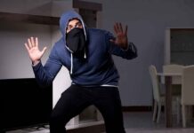 Person in hoodie and face covering raising hands indoors