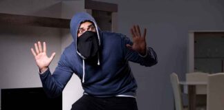 Person in hoodie and face covering raising hands indoors