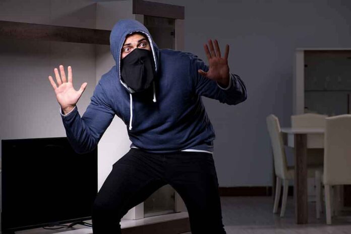 Person in hoodie and face covering raising hands indoors