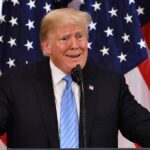 Donald Trump speaking at a podium with U.S. flags in the background