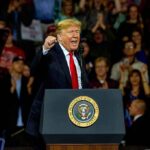 Donald Trump speaking at a rally behind a presidential podium