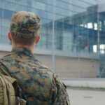soldier in camouflage with backpack outside modern glass building