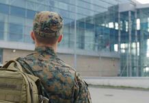 soldier in camouflage with backpack outside modern glass building