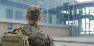 soldier in camouflage with backpack outside modern glass building