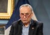 Charles Ellis Schumer wearing red glasses and a dark blazer
