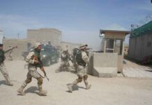 Soldiers in desert uniforms run past a checkpoint amid dust
