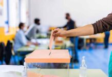 Dems Take Early Edge In Mail-in- Ballots Hand casting ballot into a box at a polling station