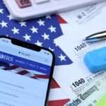 IRS Checkbox Sparks Immigration Panic Smartphone showing IRS website on top of tax forms and office supplies