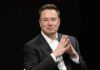 Elon Musk seated in a black suit with hands clasped