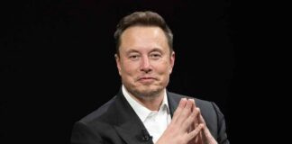 Elon Musk seated in a black suit with hands clasped