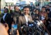 Zohran Mamdani speaks at a press conference; Julia Bacha is visible among the crowd