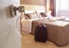 Hotel room key in door with suitcase by bed
