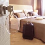 Hotel room key in door with suitcase by bed