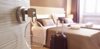 Hotel room key in door with suitcase by bed